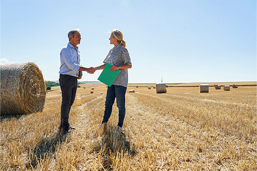A banker and a farmer shaking hands in a field